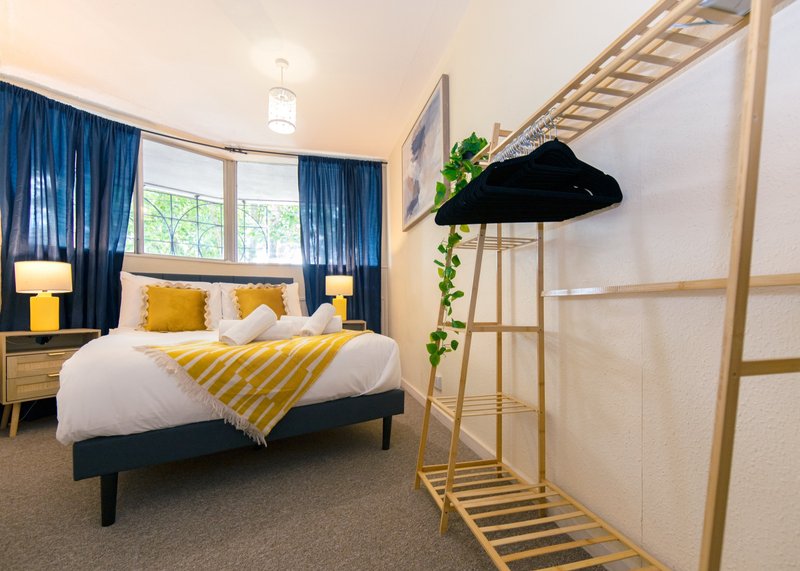 Modern bedroom with double bed, yellow bedding, blue curtains, wooden ladder shelf and pendant light