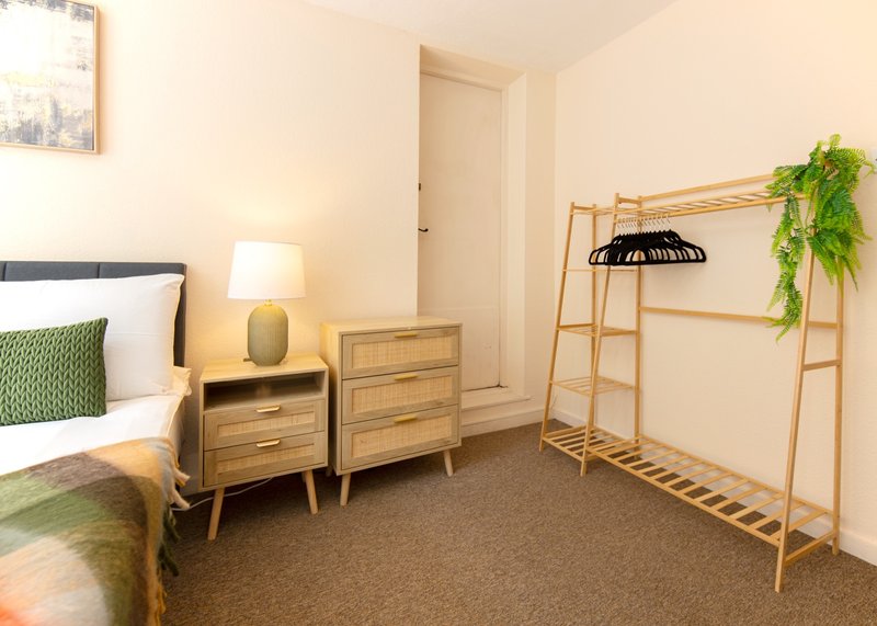 Bedroom with double bed, wooden nightstands, lamp, wooden clothing rack and green plant