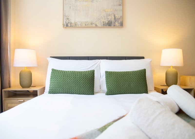 Bedroom with double bed, green pillows, white bedding, and bedside lamps