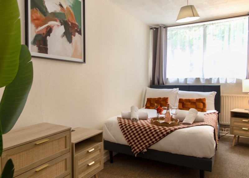 Bedroom with double bed, wooden dresser, framed wall art, and large window with natural light