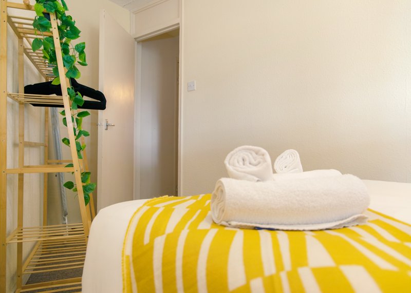 Bright bedroom with yellow striped bedding, rolled towels, potted plant and wooden ladder shelf