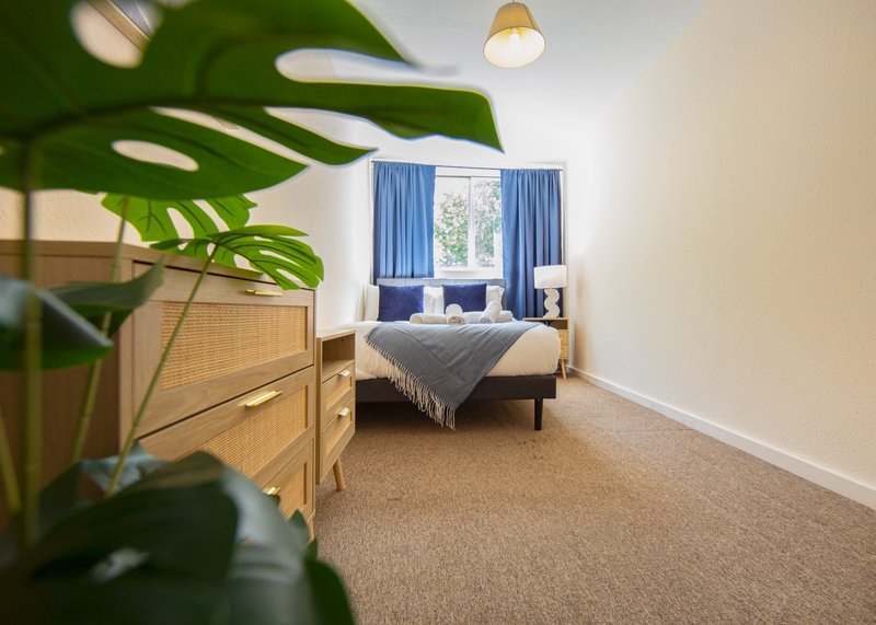 Bright bedroom with double bed, wooden furniture, blue curtains and potted plant