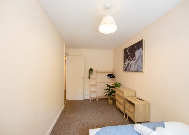 Bedroom with single bed, wooden storage unit, potted plant and wall art