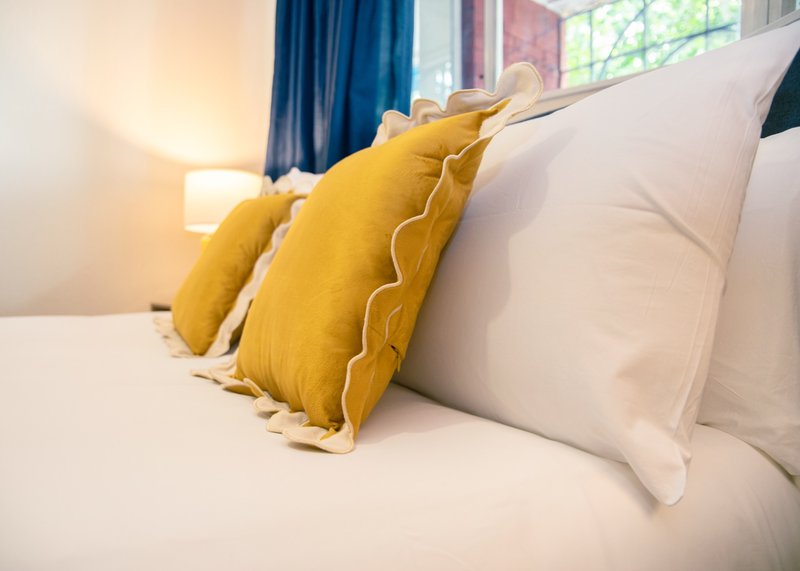 Bedroom with white bedding, yellow decorative cushions, and blue curtains by window