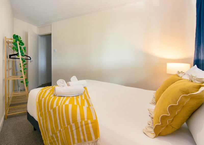 Bedroom with double bed, yellow striped throw, decorative pillows and bedside lamp