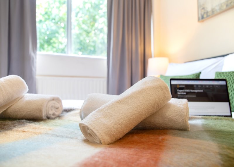 Bedroom with rolled towels on bed, laptop, window with curtains and garden view