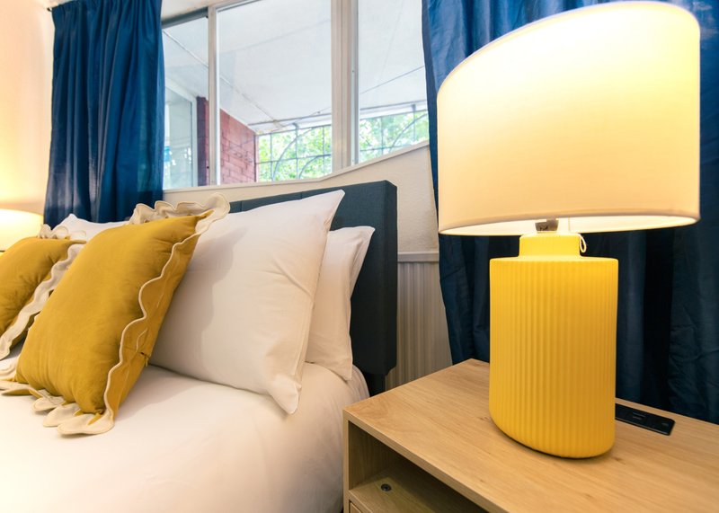 Bright bedroom with double bed, yellow cushions, bedside lamp and blue curtains