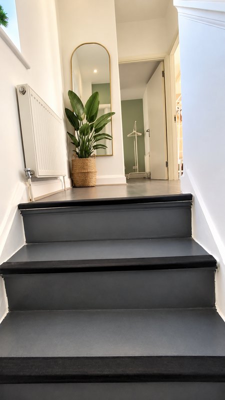 Modern staircase with black steps, potted plant, round mirror and white walls