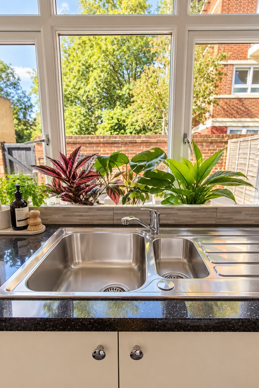 Modern kitchen sink with stainless steel basin, plants on windowsill, large window overlooking garden