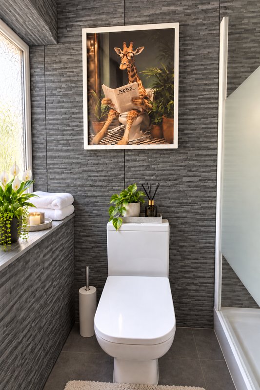 Modern bathroom with toilet, sink, potted plants and framed giraffe artwork on tile wall