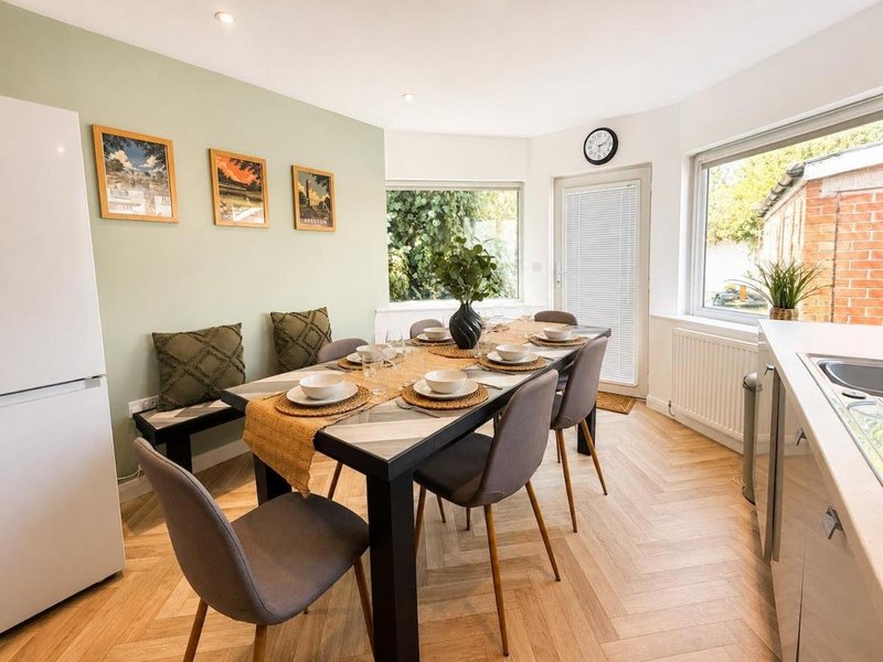 Modern dining room with black table, grey chairs, wooden floor and kitchen area