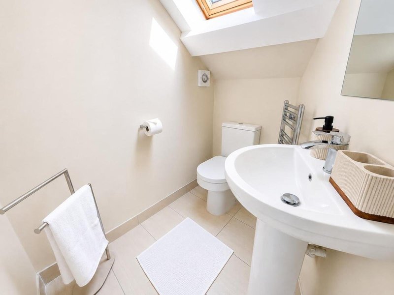 Clean modern bathroom with pedestal sink, toilet, towel rail and skylight