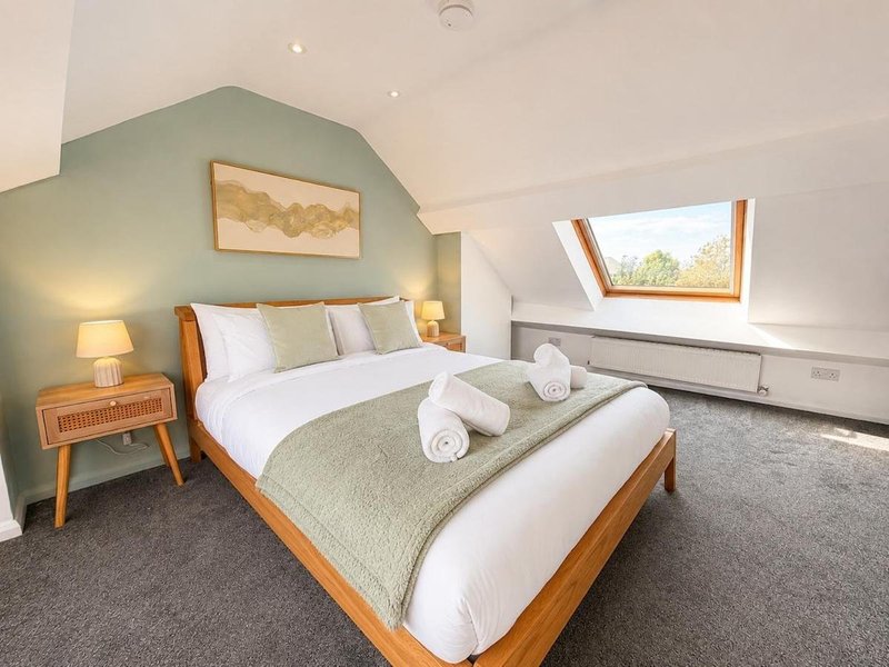 Bright bedroom with wooden bed, sage green accent wall, bedside table and skylight window