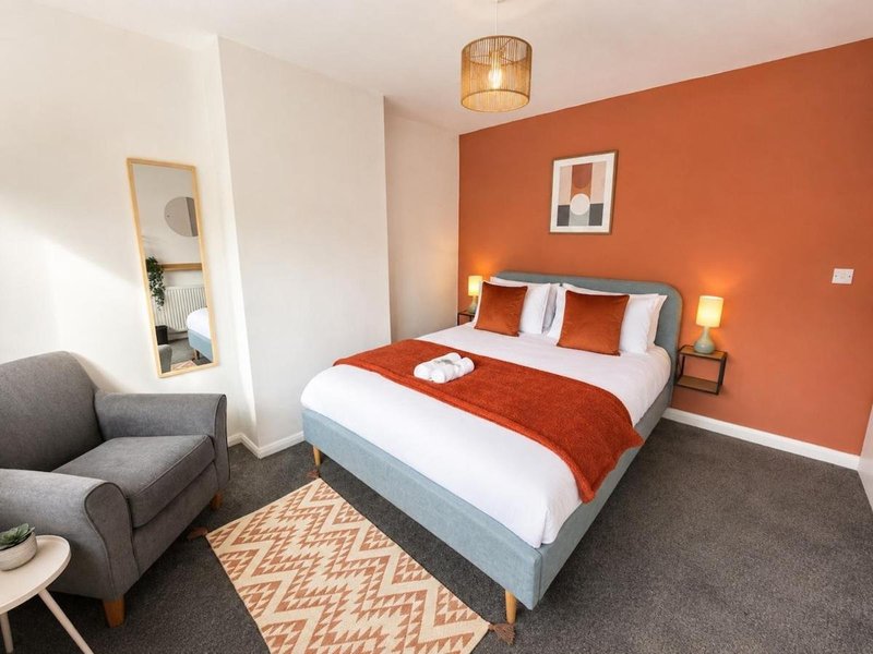Modern bedroom with double bed, orange accent wall, armchair, and pendant light