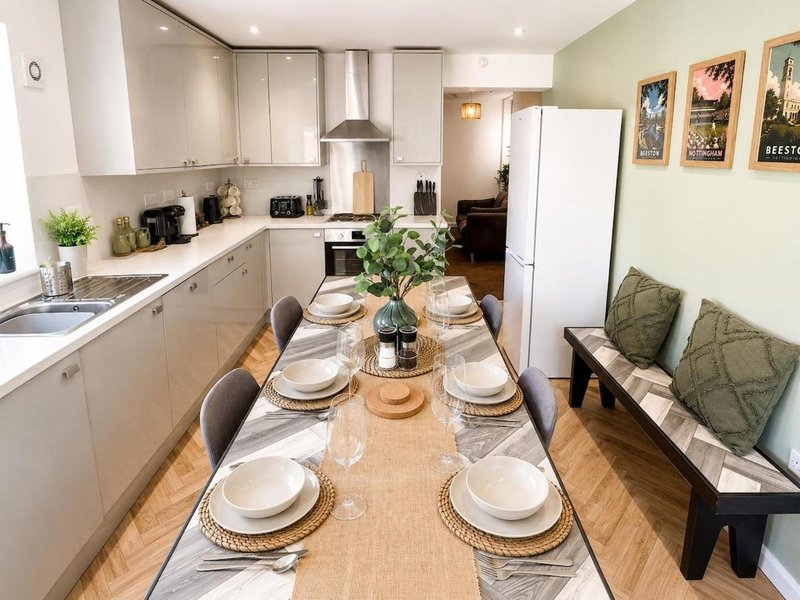 Modern kitchen-diner with white cabinetry, dining table set for meal, green accent wall and seating area