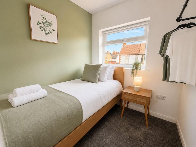Compact bedroom with single bed, wooden nightstand, green accent wall and window view