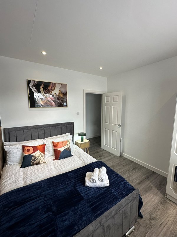 Modern bedroom with dark upholstered bed, colorful cushions, white bedding and recessed ceiling lights