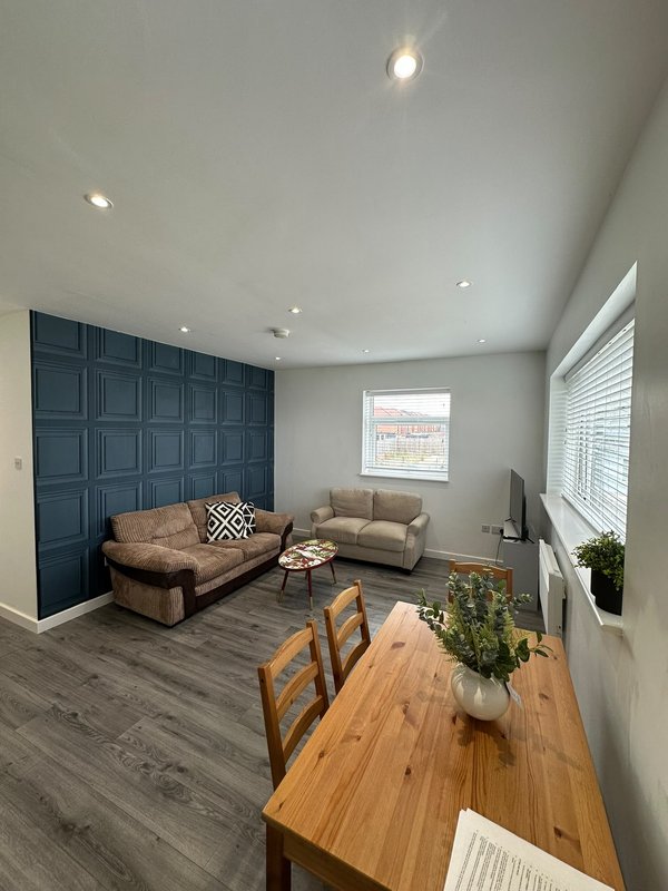 Modern living room with navy feature wall, beige sofa, wooden dining table and chairs, potted plants