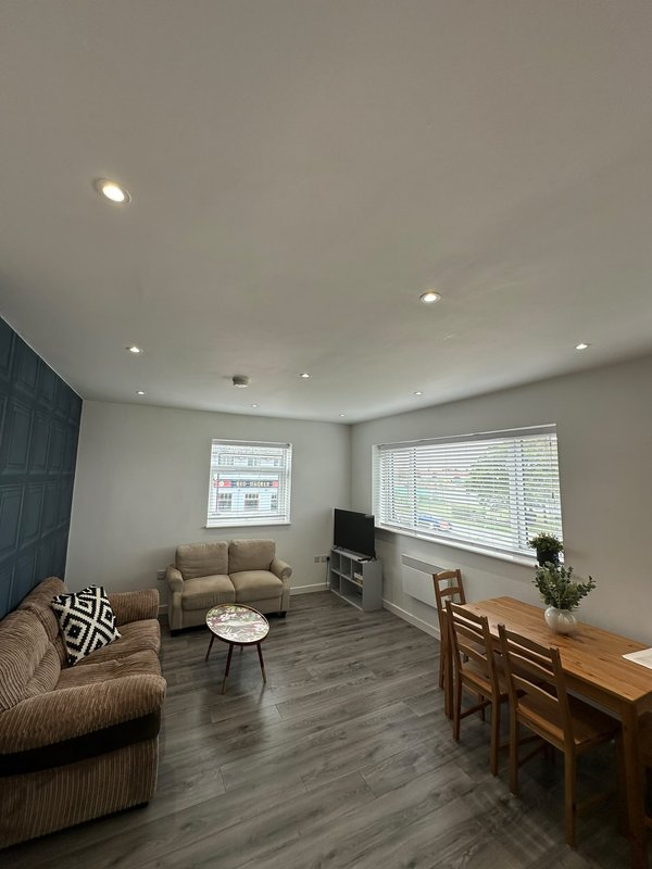 Open-plan living room with beige sofa, wooden dining table, TV stand and windows