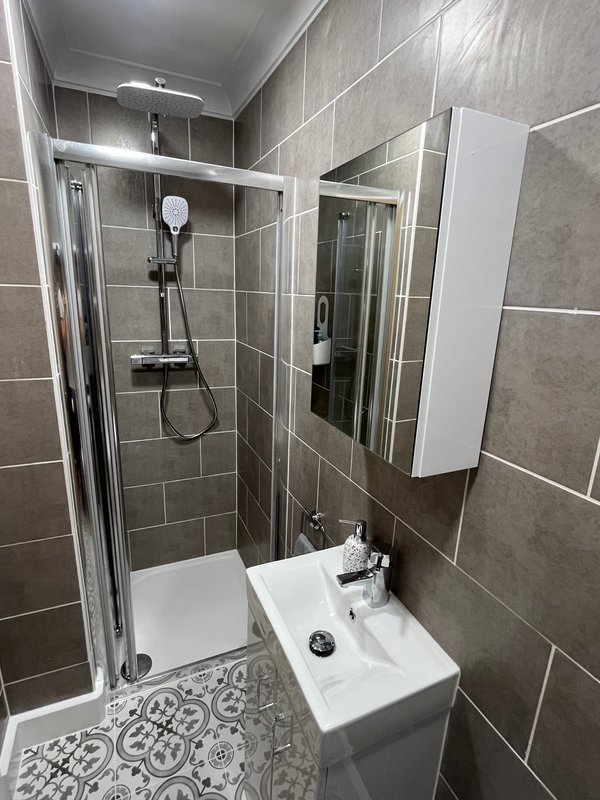 Modern bathroom with grey tile walls, shower cubicle, white sink and mirror cabinet