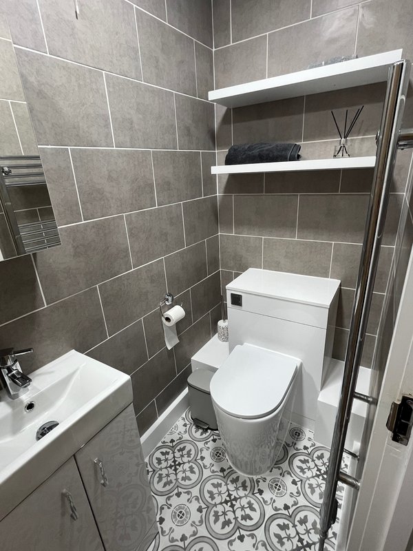 Modern bathroom with grey tile walls, white toilet, sink, and shower enclosure with shelving