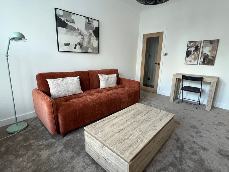 Living room with rust-colored sofa, wooden coffee table, floor lamp and wall art