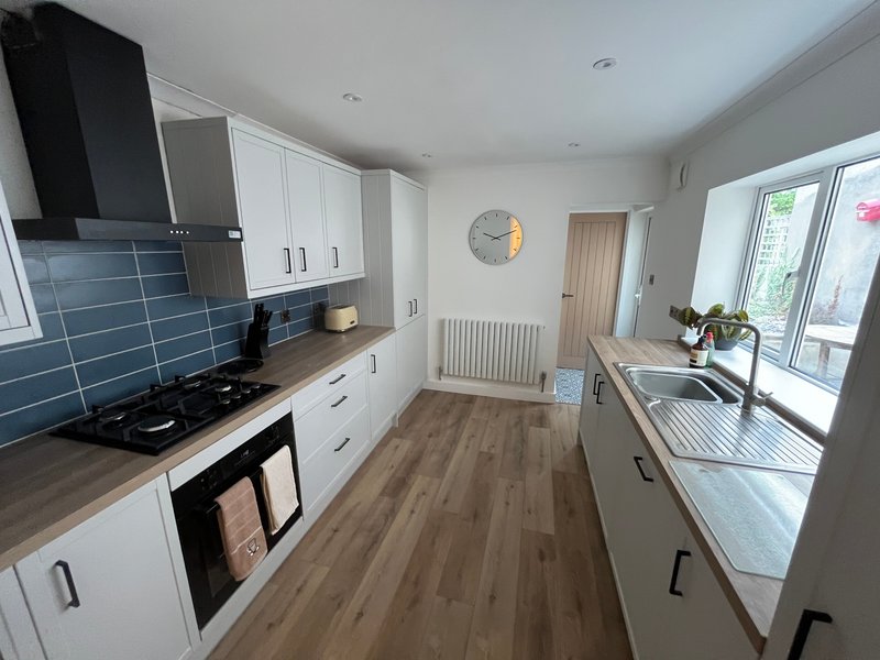Modern kitchen with white cabinetry, blue tile backsplash, wooden flooring and garden view