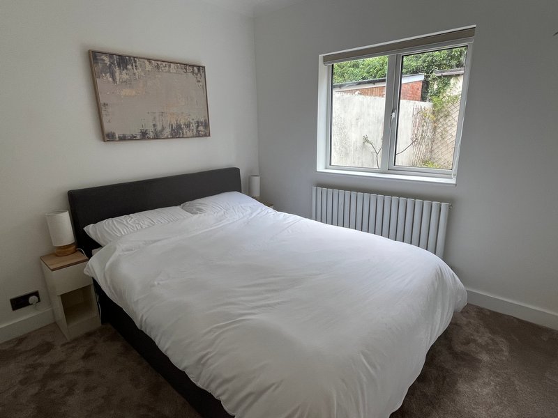 Bedroom with double bed, black headboard, white bedding, and window overlooking garden