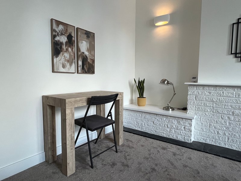 Modern home office with wooden desk, black chair, white brick feature wall and framed artwork