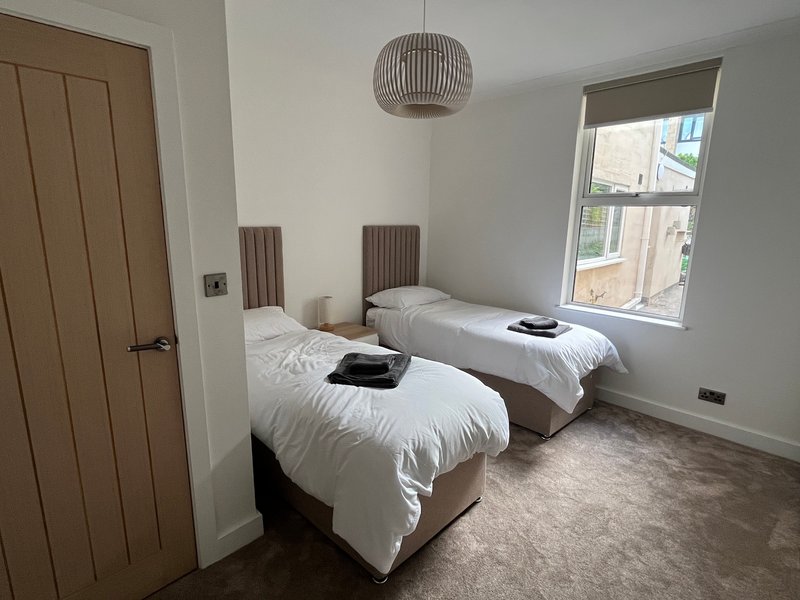 Twin bedroom with two single beds, pendant light, wooden door and window with city views