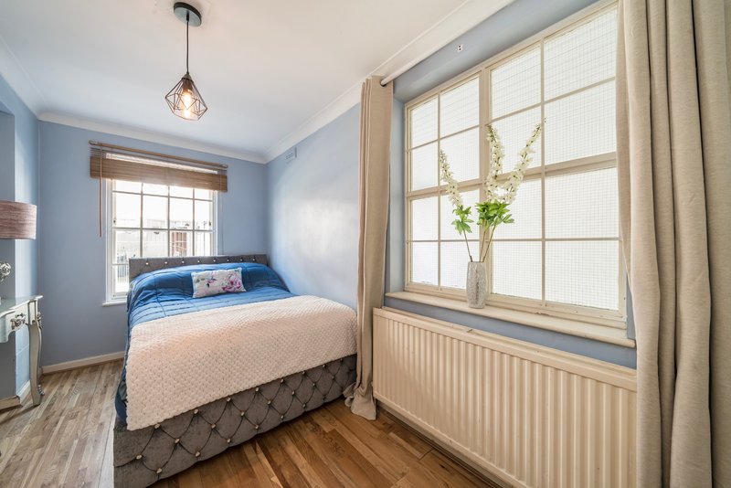 Bright bedroom with double bed, blue headboard, wooden floor and large windows