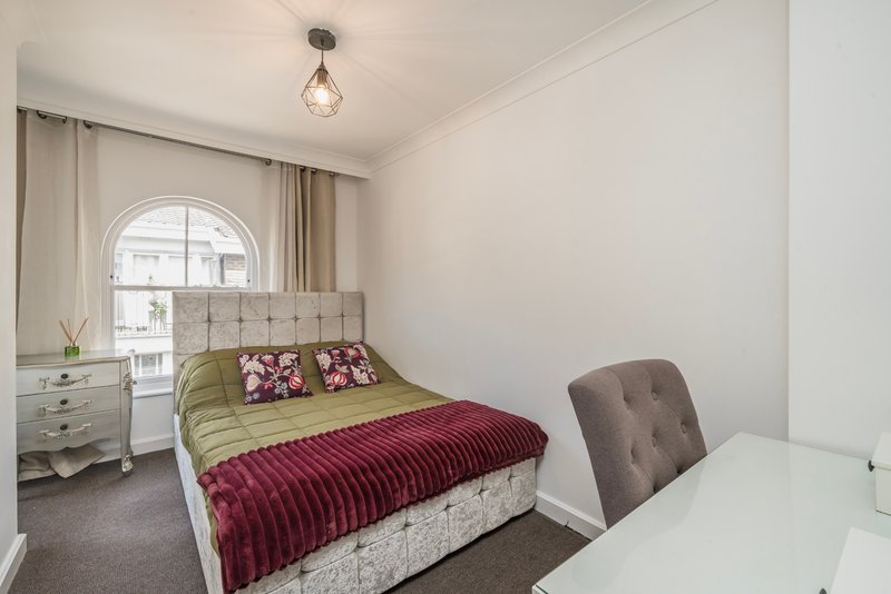 Bedroom with double bed, upholstered headboard, burgundy bedding, arched window, desk and chair