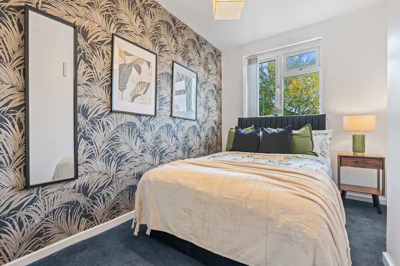 Modern bedroom with patterned wallpaper, double bed, wooden bedside table and large window