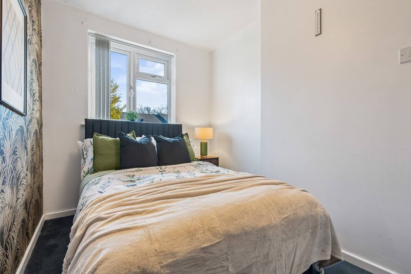 Bright bedroom with double bed, striped bedding, cushions, and large window with garden view