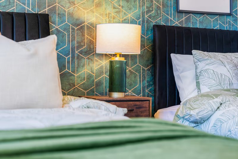 Modern bedroom with black upholstered headboard, geometric wallpaper, bedside lamp and white pillows