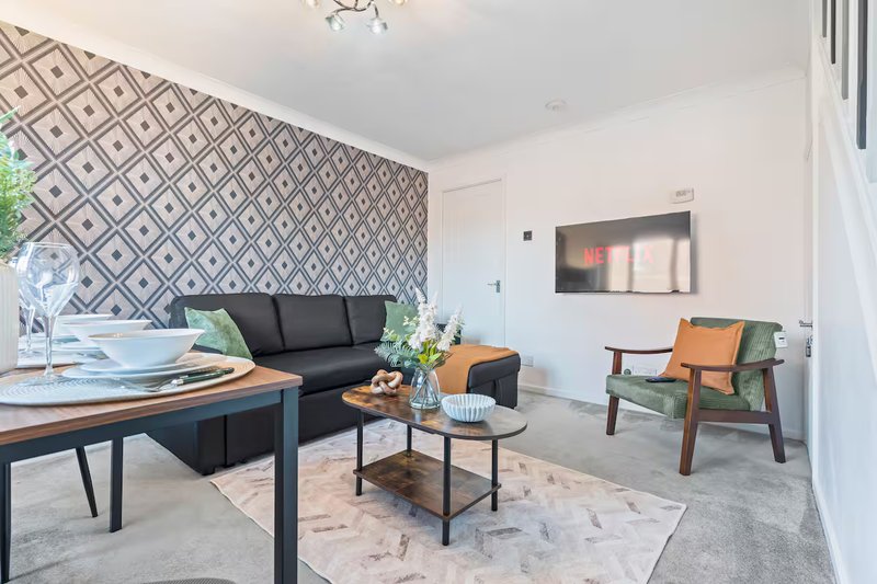 Modern living room with geometric wallpaper, black sofa, wooden dining table, and mid-century chair