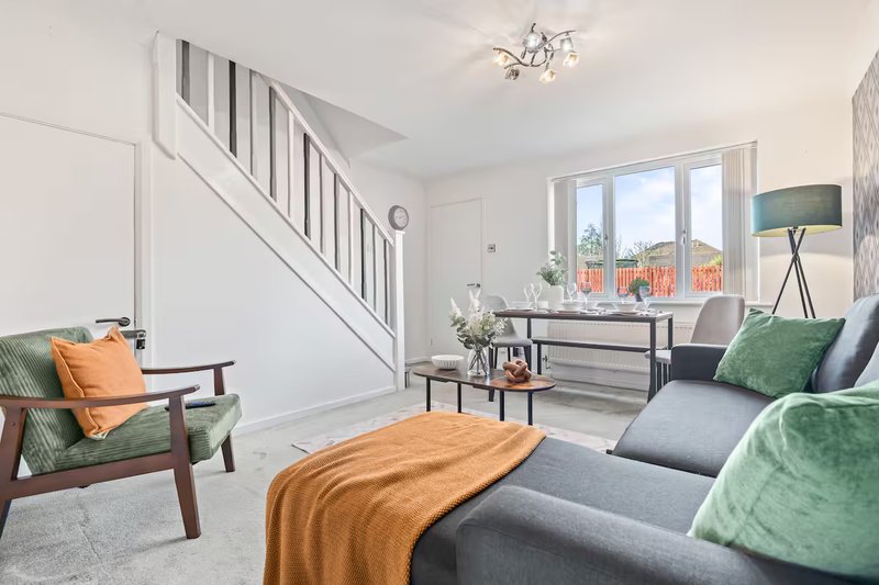 Open-plan living room with staircase, sofa, armchair, and window view of garden