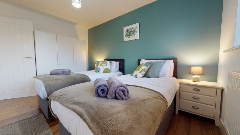 Bright twin bedroom with teal feature wall, two beds, rolled towels, and bedside lamps