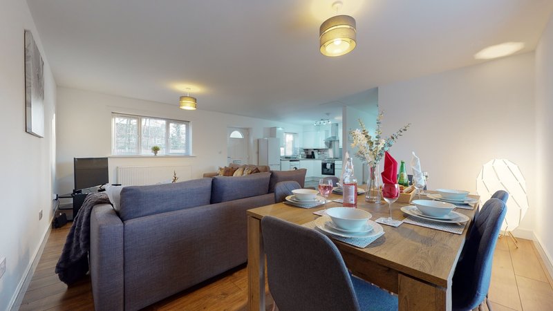 Open-plan living and dining area with blue sofa, wooden dining table, kitchen, and bright windows
