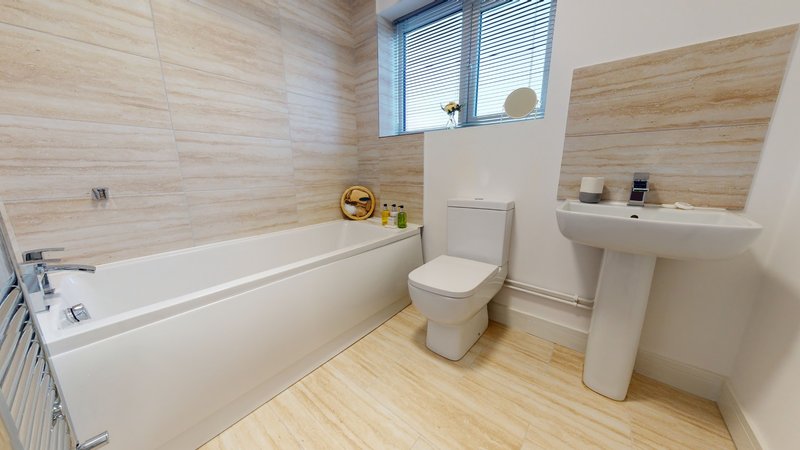 Modern bathroom with white bathtub, toilet, pedestal sink and wooden flooring