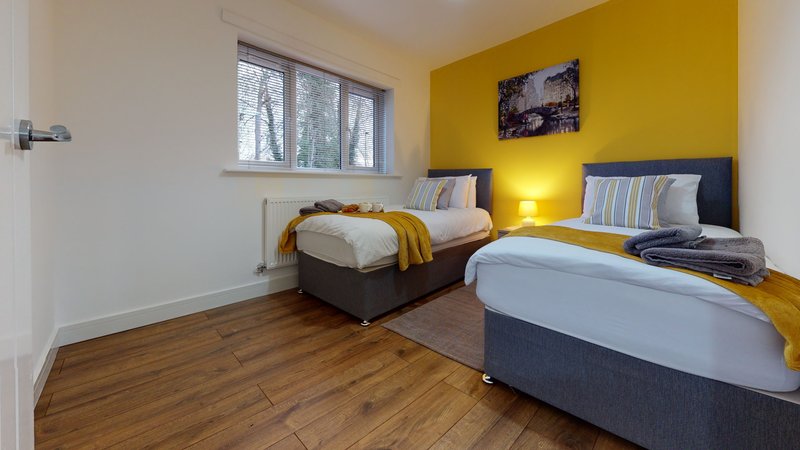 Bright yellow bedroom with two single beds, wooden floor, window and wall art