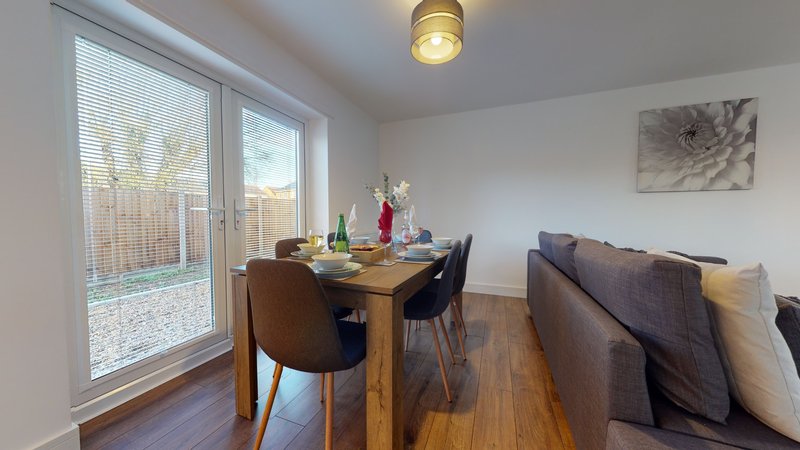 Open-plan dining and living area with wooden table, chairs, sofa, and patio doors
