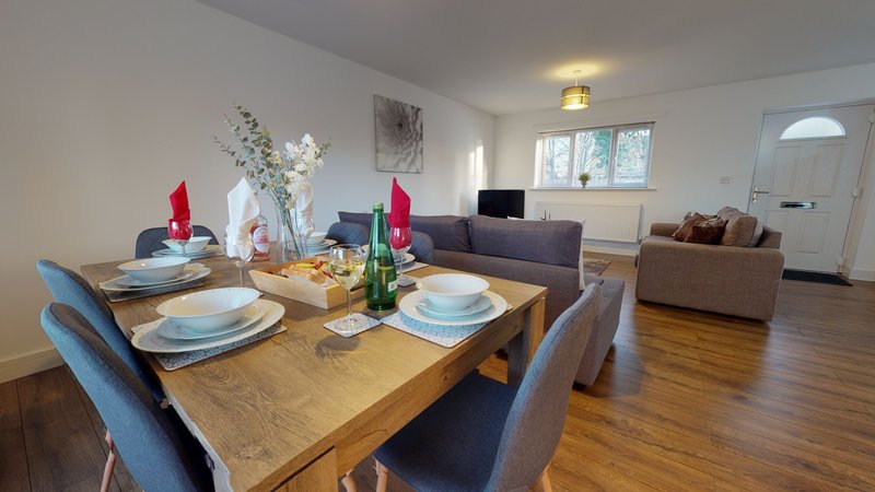 Open-plan living area with wooden dining table, place settings, and sofas visible in background
