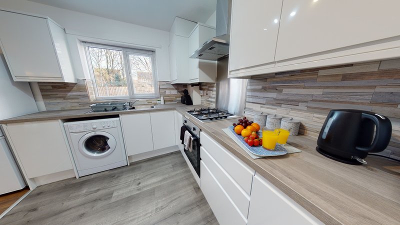 Modern kitchen with white cabinets, gas range, washing machine, and wood-effect countertops.
