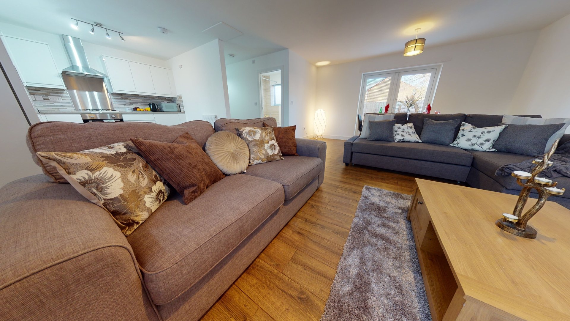 Open-plan living room with brown sofa, dark blue sofa, wooden table and kitchen area
