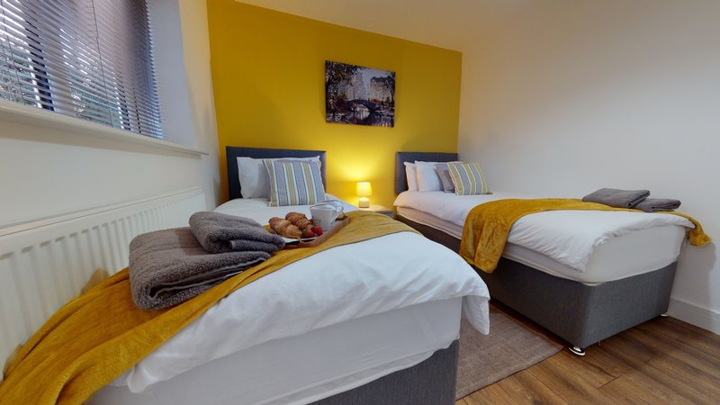Bright bedroom with two single beds, yellow accent wall, wooden floor and bedside lamps