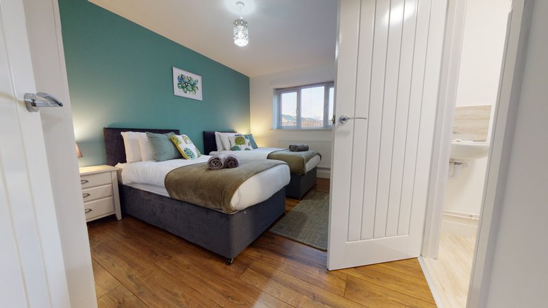 Bedroom with double bed, teal accent wall, wooden floor and ensuite bathroom