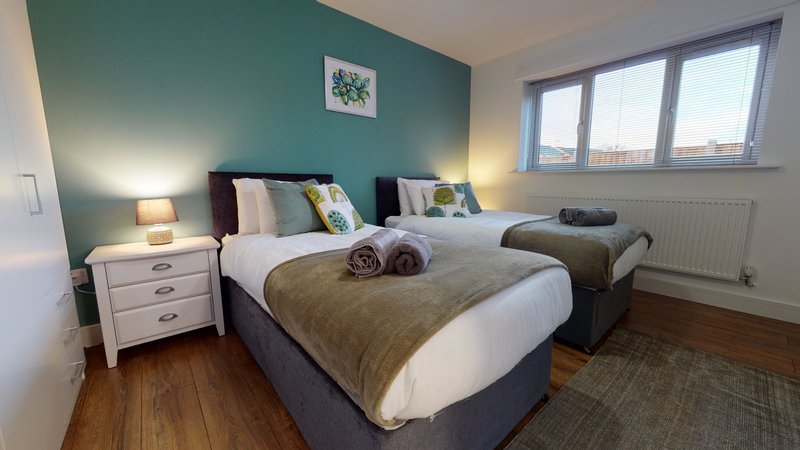 Bright bedroom with two double beds, teal accent wall, wooden floor and large windows