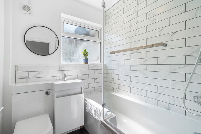Modern bathroom with white subway tiles, toilet, pedestal sink, round mirror and bathtub