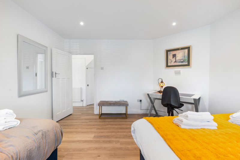 Bright bedroom with two beds, desk, chair, wooden floor and white walls